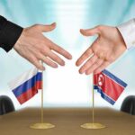 Two hands reaching over Russian and North Korean flags.
