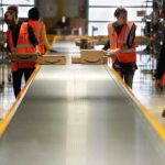 Workers in warehouse sorting packages on conveyor.