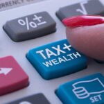 Finger pressing "TAX + WEALTH" calculator button.