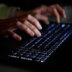 Hands typing on a backlit keyboard in darkness