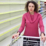 Woman in pink sweater with empty store shelves.