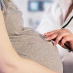 Doctor uses stethoscope on pregnant woman's belly.