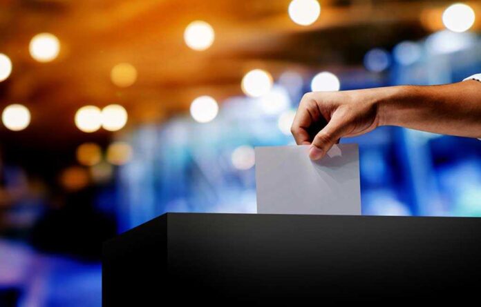 1666176196 featured image Hand placing ballot in voting box.