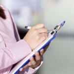 Person writing on a clipboard with a pen