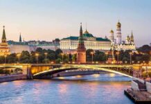 Illuminated bridge and Kremlin complex across river at twilight.