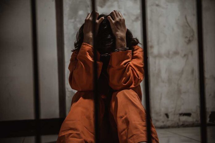 1484320151 featured image Person in orange jumpsuit sitting behind bars, handcuffed.