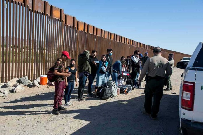 Group of people at border wall with patrol agents.