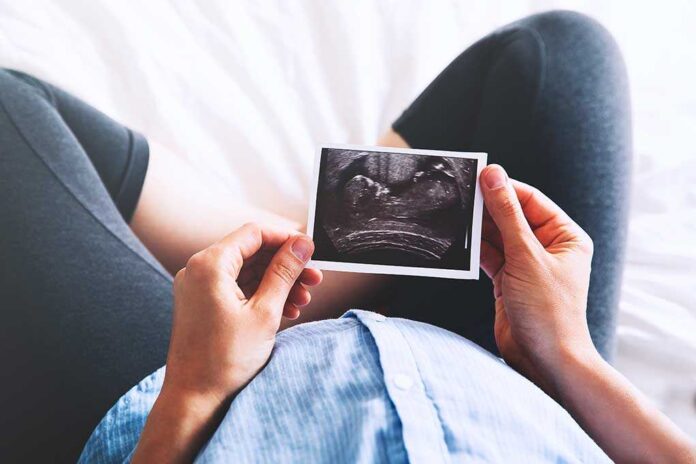 626242508 featured image Person holding ultrasound image over pregnant belly