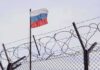 Barbed wire fence with Russian flag in background
