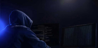 Hooded figure using dual monitors in dark room