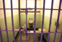 Interior of a prison cell with a toilet, sink, and metal bars