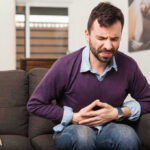 Belly Rub Warning: Beware the Unplanned Poop! Man sitting on couch, holding stomach in pain