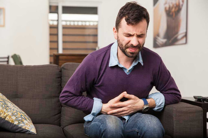 Man sitting on couch, holding stomach in pain