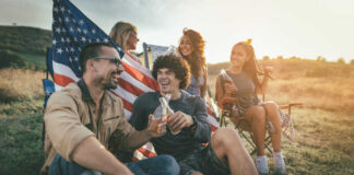 Group of friends enjoying drinks outdoors with an American flag in the background