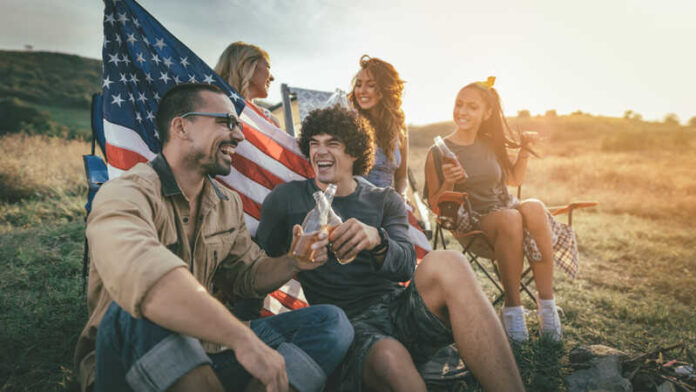 Group of friends enjoying drinks outdoors with an American flag in the background