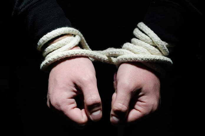 Hands tied with rope in the dark.