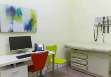 A modern medical examination room with a computer, phone, and examination table