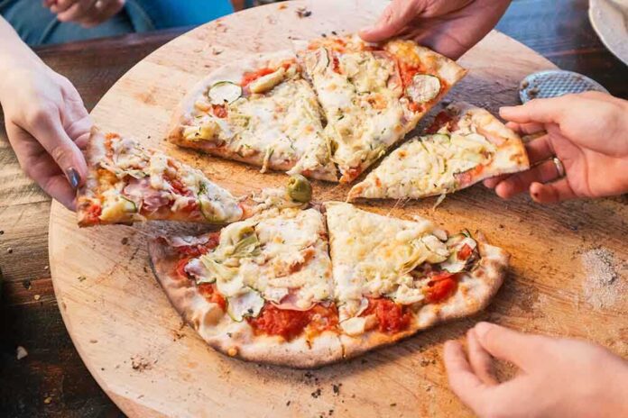 People sharing slices of pizza on a wooden board