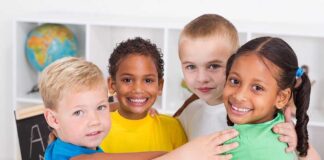 Four children of diverse backgrounds smiling and hugging each other in a classroom