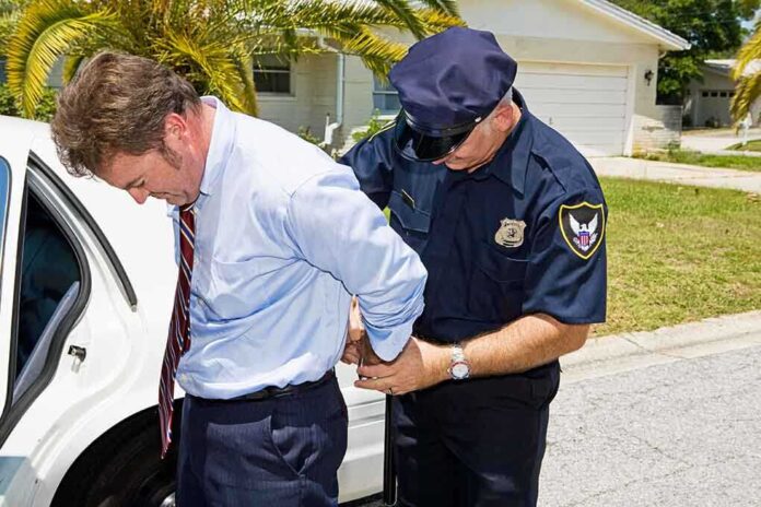 shutterstock_17843134.jpg A police officer handcuffing a man in formal attire outside a police car