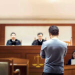 Democrat Staffer Impersonates Lawyer—BUSTED! Man stands in courtroom before judges and stenographer.