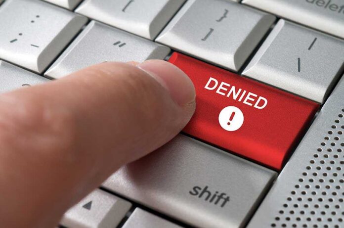A finger pressing a red DENIED button on a computer keyboard