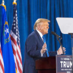 Obama Judge BACKS TRUMP — Major WIN Person speaking at podium with flags in background.