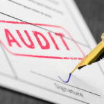 Audit stamp and pen signing a document.