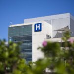 Deadly Fungus INVADES 27 States Modern hospital building with a prominent H sign against a clear blue sky
