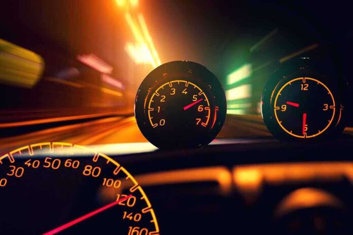 Close-up of a car dashboard with speedometer and tachometer illuminated at night