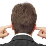 Man in a suit with his hands covering his ears, viewed from the back