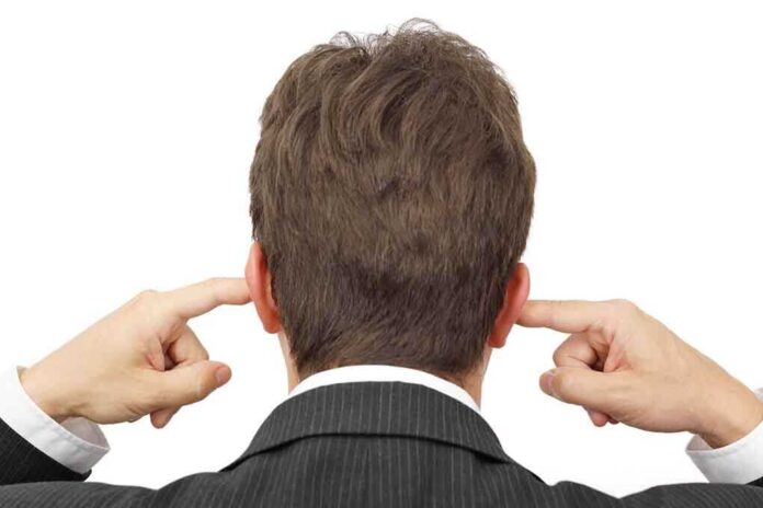 Man in a suit with his hands covering his ears, viewed from the back