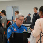 TSA PreCheck Morphs Into ‘BIG BROTHER’ TSA agent checks passengers documents at airport security.