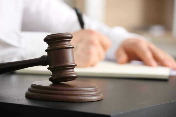 2454469737 Judges gavel on desk with person writing.