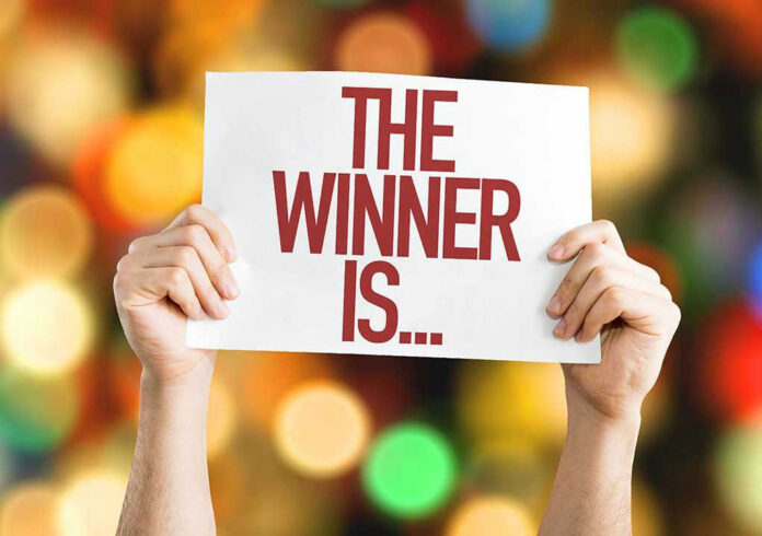 Hands holding a sign reading The Winner Is...