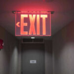 Trump TORCHES 66 Global Bodies in One Swipe Red illuminated exit sign in a hallway.