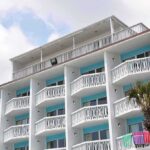 Agents Doxxed! Hotel’s Shocking LEAK Exterior view of a beachfront hotel with balconies and colorful towels hanging