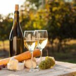 French WINE Faces Devastation A bottle of white wine, two glasses, cheese, and grapes on a wooden table in a vineyard