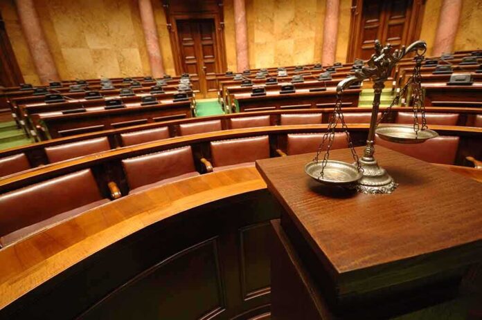 A courtroom with empty seats and a scale of justice in the foreground