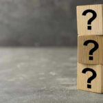 Three wooden blocks with black question marks stacked.