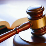 Gavel resting on sounding block beside open book.