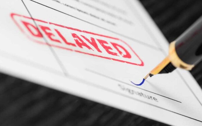A close-up of a document with a red 'DELAYED' stamp and a fountain pen poised to sign