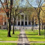 Students walking on a university campus with autumn trees and a historic building in the background