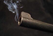 Close-up of a gun barrel emitting smoke against a black background