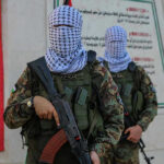 Masked soldiers holding rifles in front of a monument.