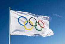 Olympic flag waving against clear blue sky.