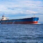 Iran Burns Ships in Hormuz Chaos A large cargo ship sailing on the ocean under a blue sky