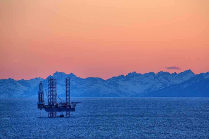 shutterstock_139270961.jpg An oil rig in the ocean with a backdrop of mountains during sunset