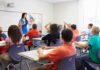 Teacher of the Year Finalist EXPOSED—Stomach-Turning Details Teacher in a blue dress instructing students in a classroom with hands raised