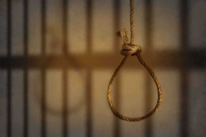A noose hanging in front of prison bars, casting shadows